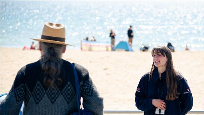Face to face fundraiser wearing a dark blue RNL jacket talking to a member of the public on the beach