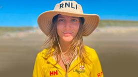 Margot Lawrence in her RNLI hat standing on a beach